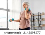 sport, fitness and healthy lifestyle concept - smiling senior woman with dumbbells exercising at home