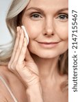 Small photo of Pretty 50s middle aged old woman holding cotton pad sponge cleansing face skin purifying with cleanser, happy mature lady removing makeup enjoy healthy clean anti age dry skincare lifting routine.