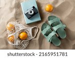 Small photo of leisure and summer holidays concept - slippers, string bag of oranges, film camera and book on beach sand