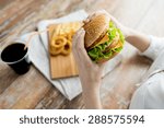 fast food, people and unhealthy eating concept - close up of woman hands holding hamburger or cheeseburger