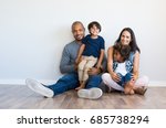 Happy multiethnic family sitting on floor with children. Smiling couple sitting with two sons and looking at camera. Mother and black father with their children leaning on wall with copy space.