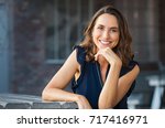 Portrait of beautiful mature woman sitting at coffee shop. Happy hispanic smiling woman sitting on a bench in outdoor cafeteria looking at camera. Portrait of carefree woman relaxing on bench.