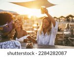 Small photo of Happy girls having fun drinking cocktails at bar on the beach - Soft focus on african girl face