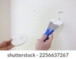 Hands with a spatula and putty against the background of a white wall, a close-up. Scatter holes on the wall