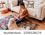 young woman working on laptop at home. cute golden retriever dog besides. healthy breakfast time. technology and lifestyle indoors