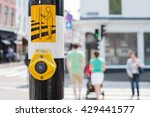 Yellow crosswalk button for pedestrian crossing, green light in background