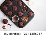 Freshly baked chocolate muffins in a baking pan on white table with ingredients