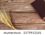 Small photo of Ripe gold barley sheaf and closed Holy Bible book on wooden table with copy space. Top view. Harvest season, grain offering, Christian thanksgiving biblical concept.