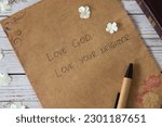 Love God, love your neighbor handwritten text verse on vintage paper with closed bible book and pen on wooden table. Christian faith and obedience to Jesus Christ, the greatest commandment concept.