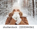 Winter walk, a young beautiful blonde in winter clothes walking in a snowy forest, a beautiful frosty day. A young woman warms her nose wrapped in a white scarf