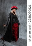 Small photo of A pretentious Gothic lady in a long leather coat and a hat with roses, uses a cane.