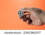 Small photo of Rolling bearings for rotating or oscillating machine components. Asian man hand holding ball bearing on orange background isolated.