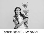 Small photo of surprised teen girl accept award on background. proud teen girl with champion cup award. teen girl hold her award champion cup isolated on yellow. teen girl receive award in studio