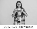 Small photo of smiling teen girl receive award in studio. teen girl accept award on background. proud teen girl with champion cup award. teen girl hold her award champion cup isolated on yellow