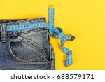 Small photo of Healthy lifestyle and dieting concept. Blue jeans with measure tape instead of belt. Close up of jeans with measure tape around waist. Upper part of denim trousers isolated on yellow background.