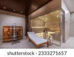 Small photo of A hall with a phytosauna-a cedar barrel, a lounge chair and a hammam bath behind a glass partition in the interior of a luxurious mansion.