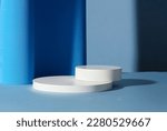 Two empty round white platforms stacked on top of each other, decorated on blue background. Empty space for display product, text and design.