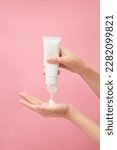 Small photo of Over a pink background, a hand model squeezing cream from a white unlabeled tube. Cosmetic product advertising