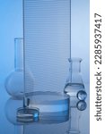 Small photo of Minimal concept with lab equipment - erlenmeyer flasks, boiling flasks and petri dish containing liquid. Transparent podium and ribbed acrylic sheets on blue background. Space for display product.