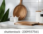 Small photo of Some kitchen amenities decorated on white tile background - spice boxes, wooden cutting board and green leaves. Blank space for product presentation. Front view, menial scene for advertising