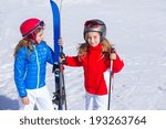 Kid girls sister in winter snow with ski equipment helmet goggles poles