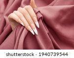Female hand with long french nail design. Long french nail polish manicure. Woman hand on red fabric background