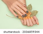 Small photo of Female hands with green and yellow autumn nail design. Female hands hold dry yellow autumn leaves. Woman hands on pale green background
