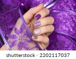 Female hand with magic nail design. Glitter purple nail polish manicure. Female model hand with perfect manicure hold purple lace fabric.