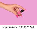 Female hand with pink nail design. Mate pink nail polish manicure. Female model hand with perfect manicure hold pink nail polish bottle on pink background. Copy space. Place for text.