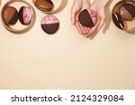 Small photo of Woman's hand with whoopie pie dessert on beige background. American traditional desserts in paper craft boxes.