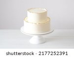 Small photo of Cake with white cream, decorated with gold confectionery sprinkles on a white background. Two-tiered white wedding cake.