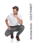 Small photo of lughing crouched smart casual man thinks and looks to side away from the camera on white background