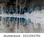Inverted colors - Beautiful snowless winter scene at partially frozen pond with bare trees and red clouds mirroring in the water surface during evening.