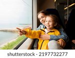 Two sister girls look out the window of a train at the sea.The girls are talking and having fun. Journey. Reflection. Vacation. Summer. Family vacation.