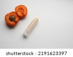 Small photo of Natural lip balms with apricot extract on white background. Lip balm or lip salve and apricots. The concept of an unnamed lipstick bottle. Commercial idea concept: Lip balm or salve and apricots