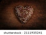 Gingerbread in the shape of a heart with chocolate icing and colored sprinkling. Valentine's Day. Wooden background.