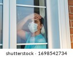 COVID-19. Sick man of coronavirus looking through the window and wearing mask protection and recovery from the illness in home. Quarantine isolation COVID19. Sick isolated at home to prevent infection