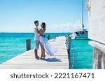 A married and happy couple looking at each other and hugging on the pier. A yacht on the turquoise ocean waters in the background