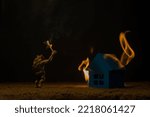 Small photo of An arsonist with a torch in the form of a monster stands in front of a burning house. Background picture.