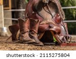 Small photo of Ranch life scenery: Muddy western boots and a cowboy hat in front of a western saddle. Western riding concept