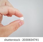 Small photo of White pill in hand. Close up to vitamin or medicine tablet between two fingers. Long, oval, white pill. Diet supplement or drug concept holden in hand. Dark background. Pain killer.