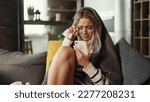 Small photo of Portrait of crying young blond woman with smartphone sitting on the couch under the blanket and reading bad news email break up message from ex-boyfriend or personal problems at home