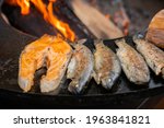 Process of grilling salmon steaks and mackerel fish on black brazier at summer local food market - close up. Outdoor cooking, barbecue, gastronomy, seafood, cookery, street food concept