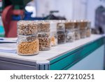 Small photo of Different kinds of pelleted compound feed, fodder in glass jars: before and after extrusion - food for domestic animals at agricultural exhibition, trade show: close up. Agriculture, husbandry concept