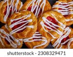 Cherry filled Danish pastry baked good with white frosting zigzagging swirl tray of pastries