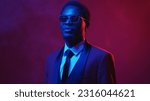 Small photo of Neon people. Masculine confidence. Dandy look. Blue pink color light portrait of proud gentleman in elegant suit glasses on dark empty space background.