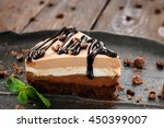 Peace of layered souffle dessert with chocolate sauce on black plate with mint leaves, on blurred wooden table