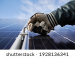 Close up of worker hand in glove holding a hex key, installing photovoltaic solar panel with blue sky on background. Electrician mounting solar photovoltaic panel system. Concept of alternative energy
