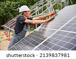 Small photo of Man in safety construction helmet mounting photovoltaic solar panel. Male technician in work gloves assembling solar modules, tightening with hex key. Concept of alternative energy sources.