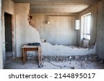 Housing redevelopment. Small table with perforator, sledgehammer placed on floor at partially destroyed inner wall. On backdrop empty walls, window, gas boiler, meter and pipes connecting them.